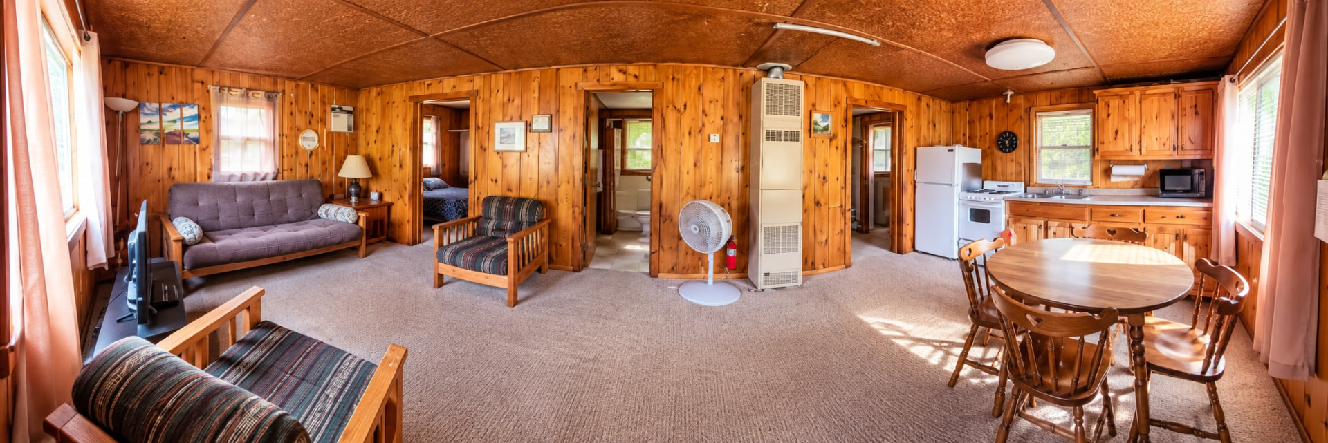 Open knotty pine living room and kitchen with dining table, futon, and full-size range and refrigerator