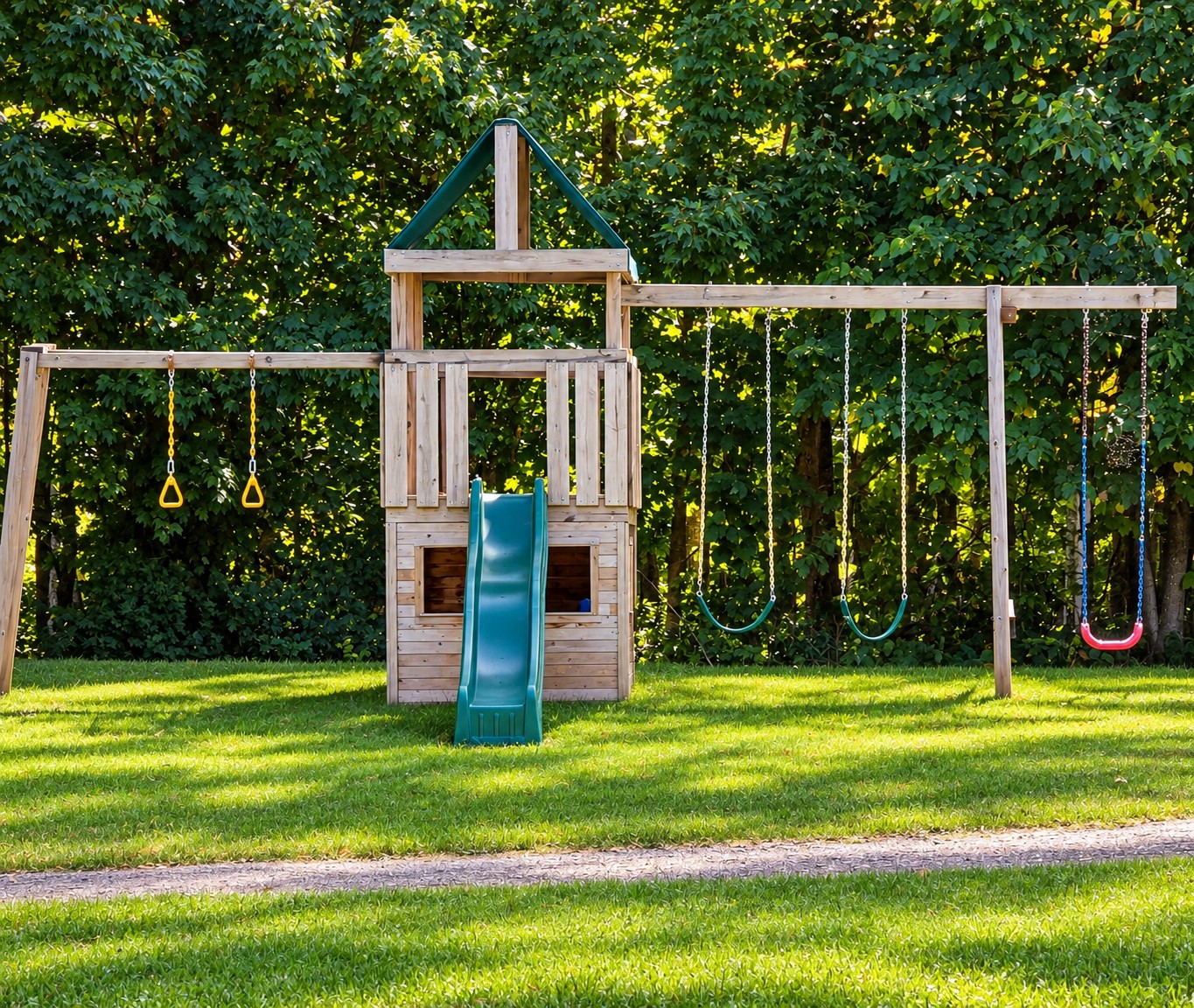 Wooden playground with a slide, swings, and rings on the resort lawn