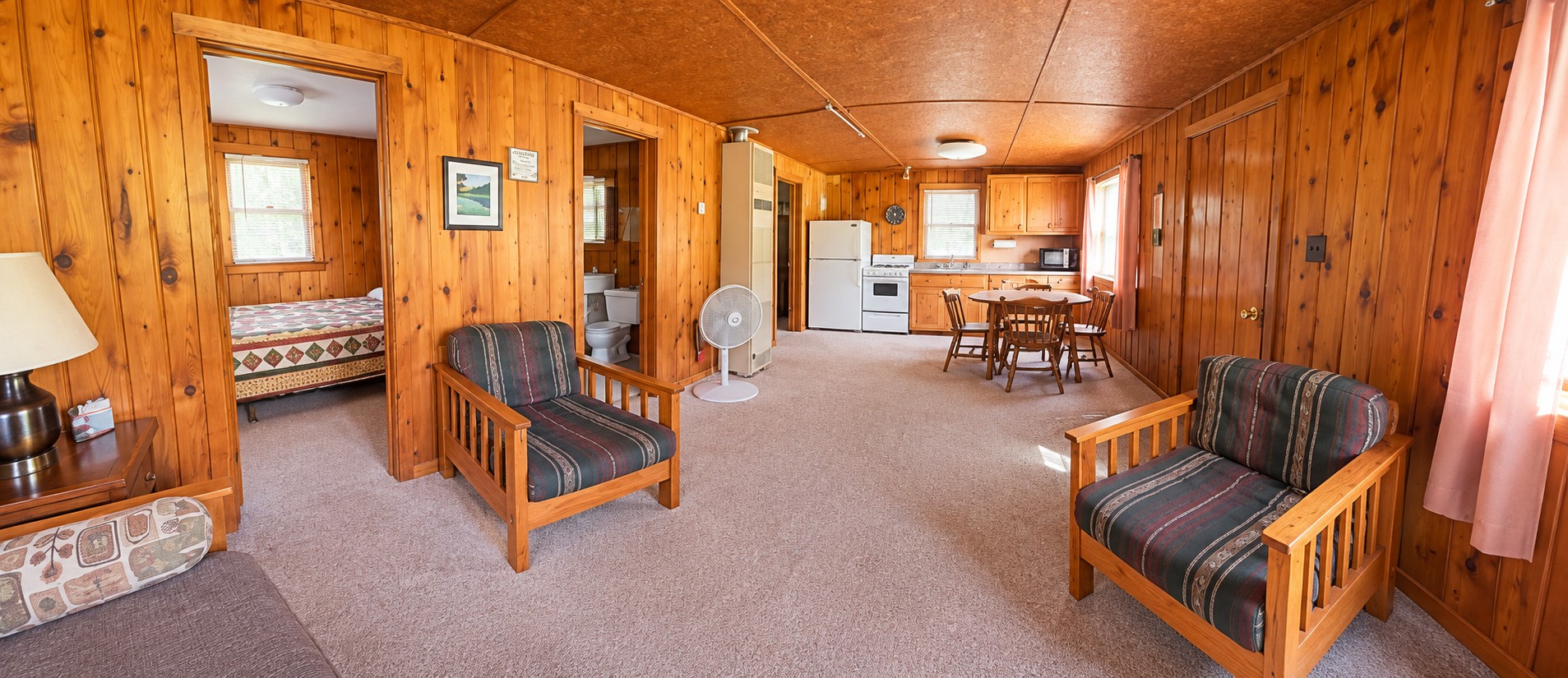 Wide view of the cabin living area with two futon chairs, a bedroom doorway, and the kitchen at the far end