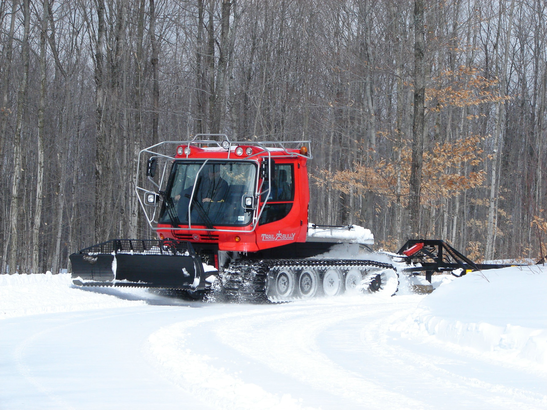 Red Trail Bully groomer packing a snowmobile trail through bare winter woods near Lake Gogebic