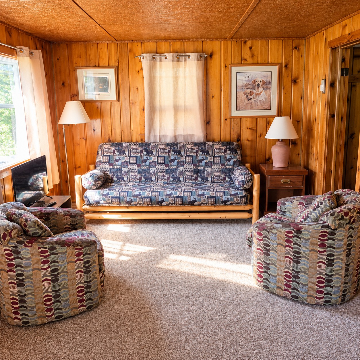 Cabin living room with a log-frame futon, two patterned armchairs, lamps, and a flat-screen TV