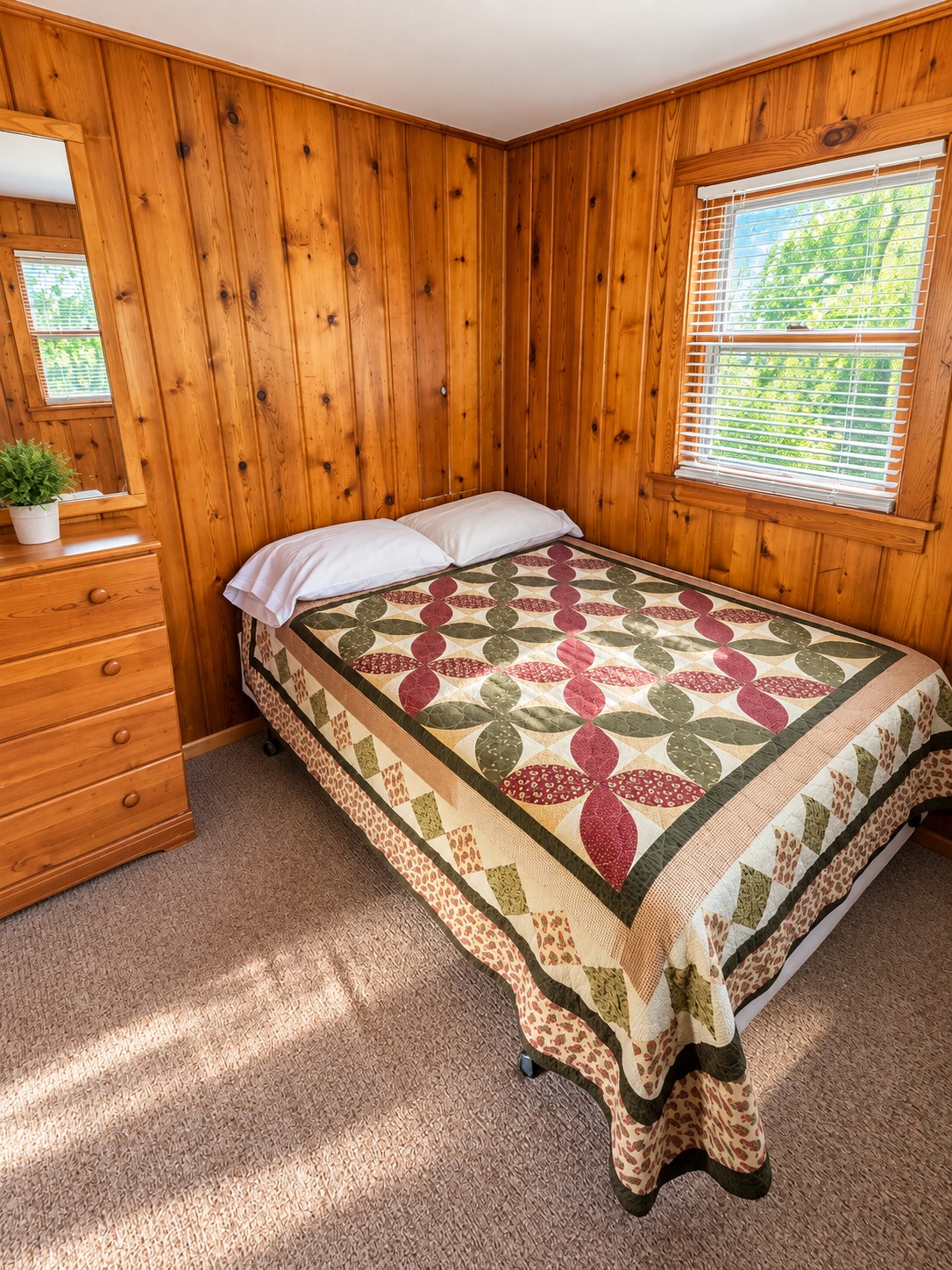 Second cabin bedroom with a quilt-covered double bed, pine dresser, and bright corner window