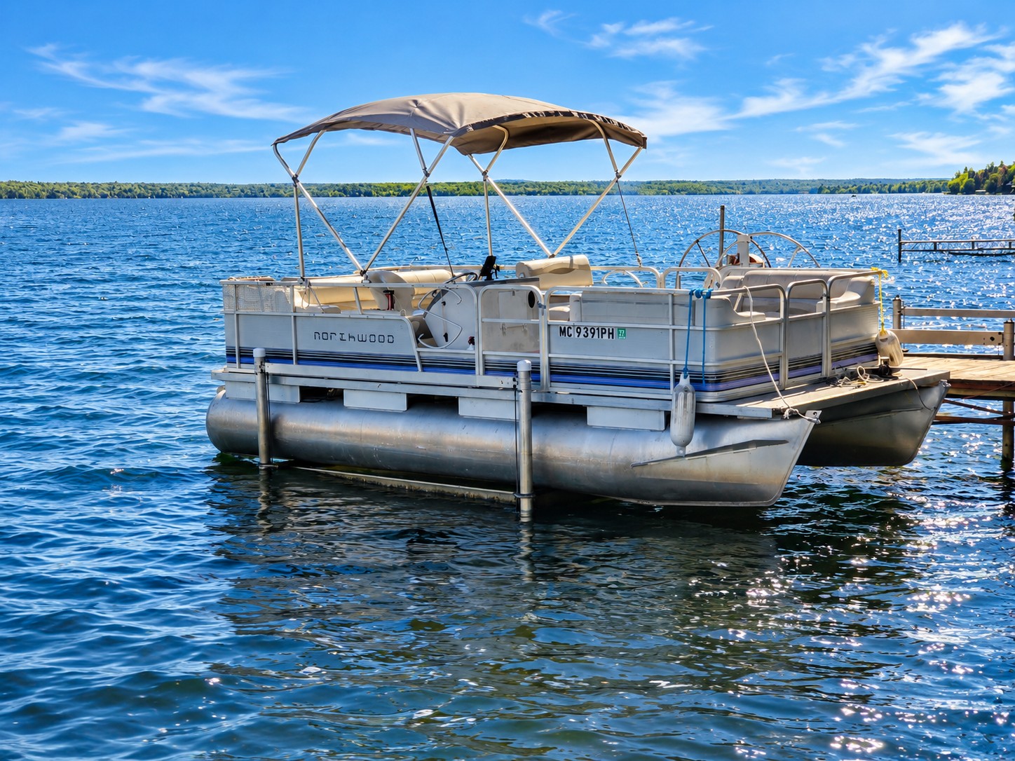 Northwood pontoon with a tan canopy tied to the dock on a sunny day on Lake Gogebic