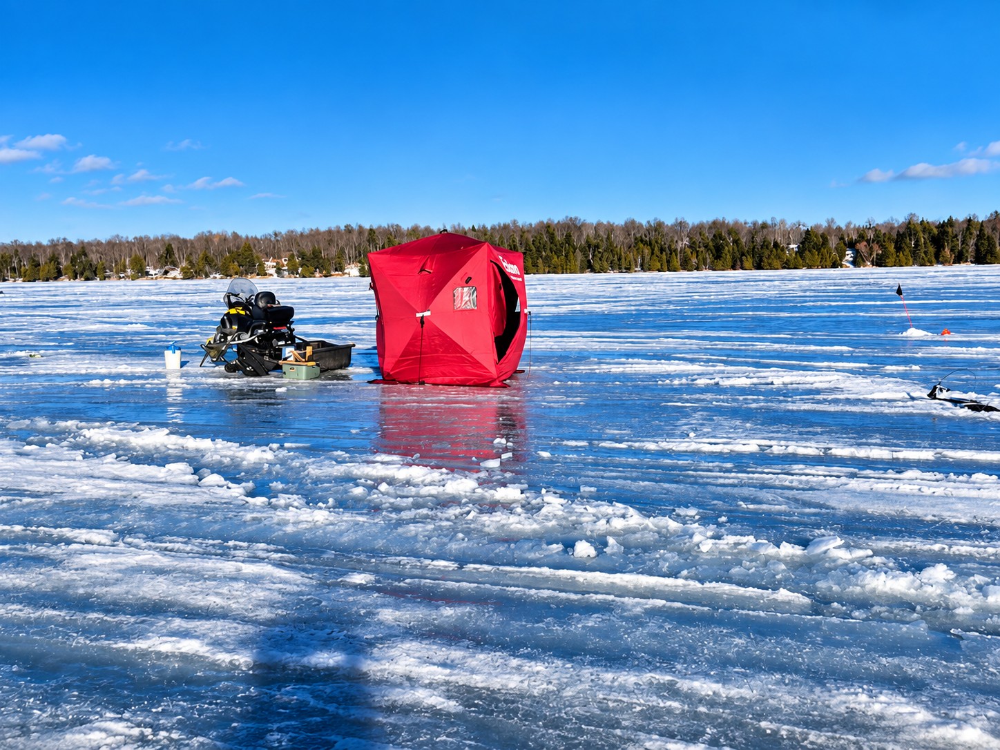 Red ice shanty and snowmobile out on the frozen surface of Lake Gogebic on a clear winter day