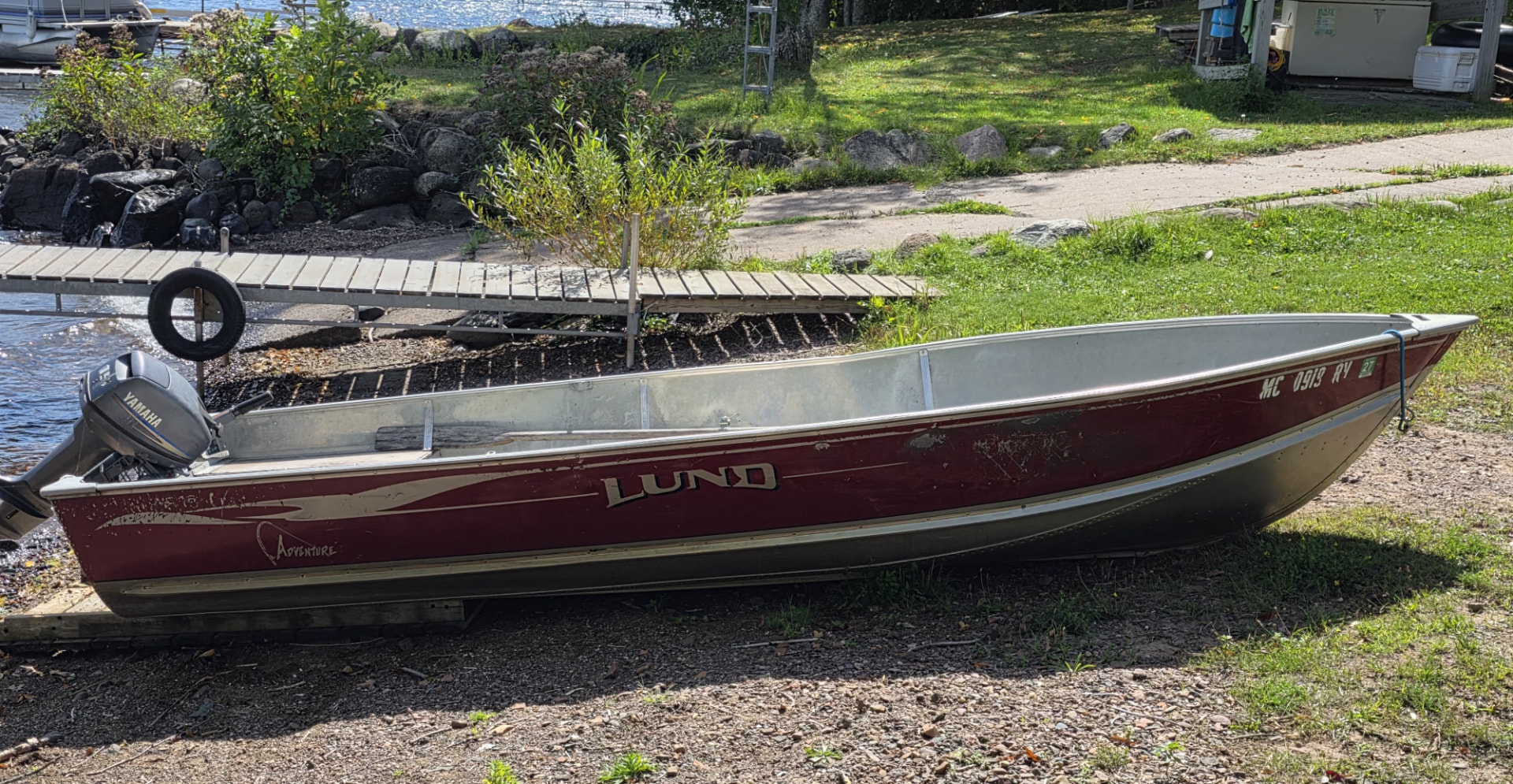 Maroon 16 foot Lund Adventure fishing boat with a Yamaha outboard motor resting on shore beside the resort dock