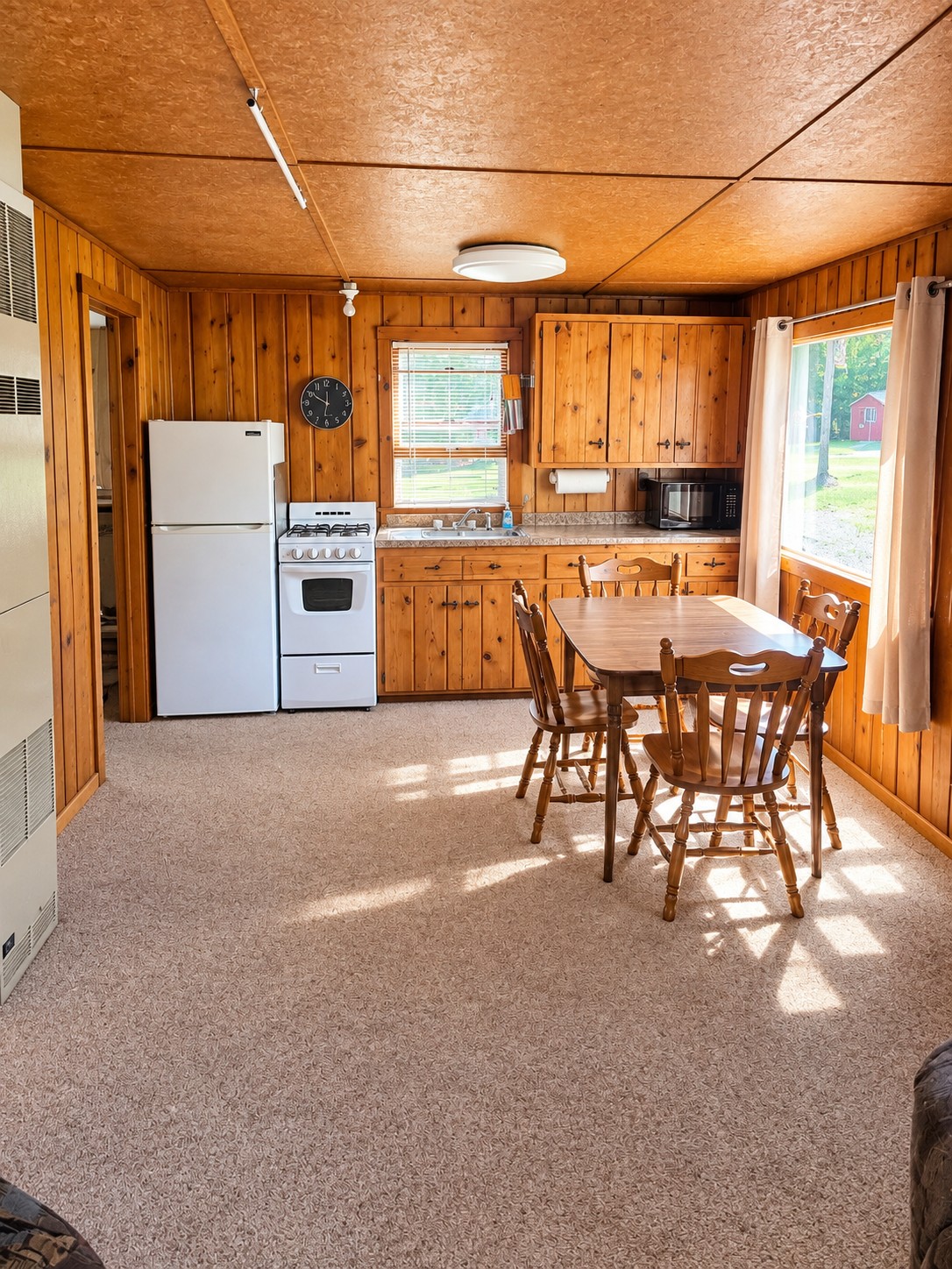Cabin kitchen with a full-size range, refrigerator, microwave, and a wood dining table for four beside a sunny window