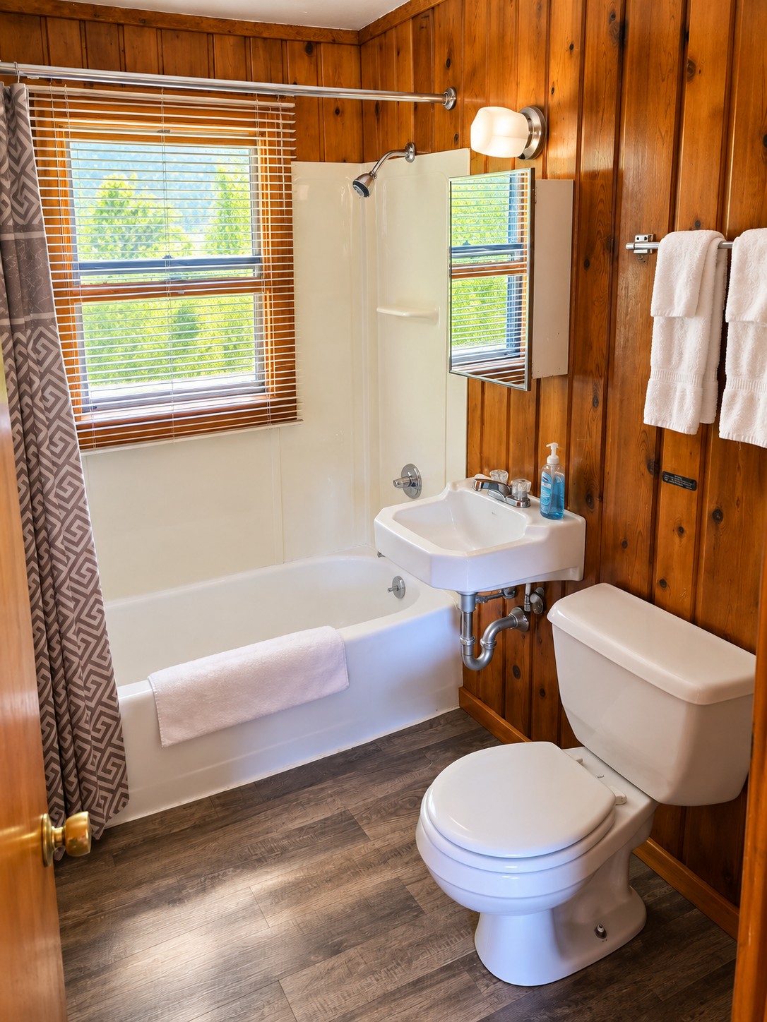 Cabin bathroom with a white tub and shower, sink, medicine cabinet mirror, and fresh white towels
