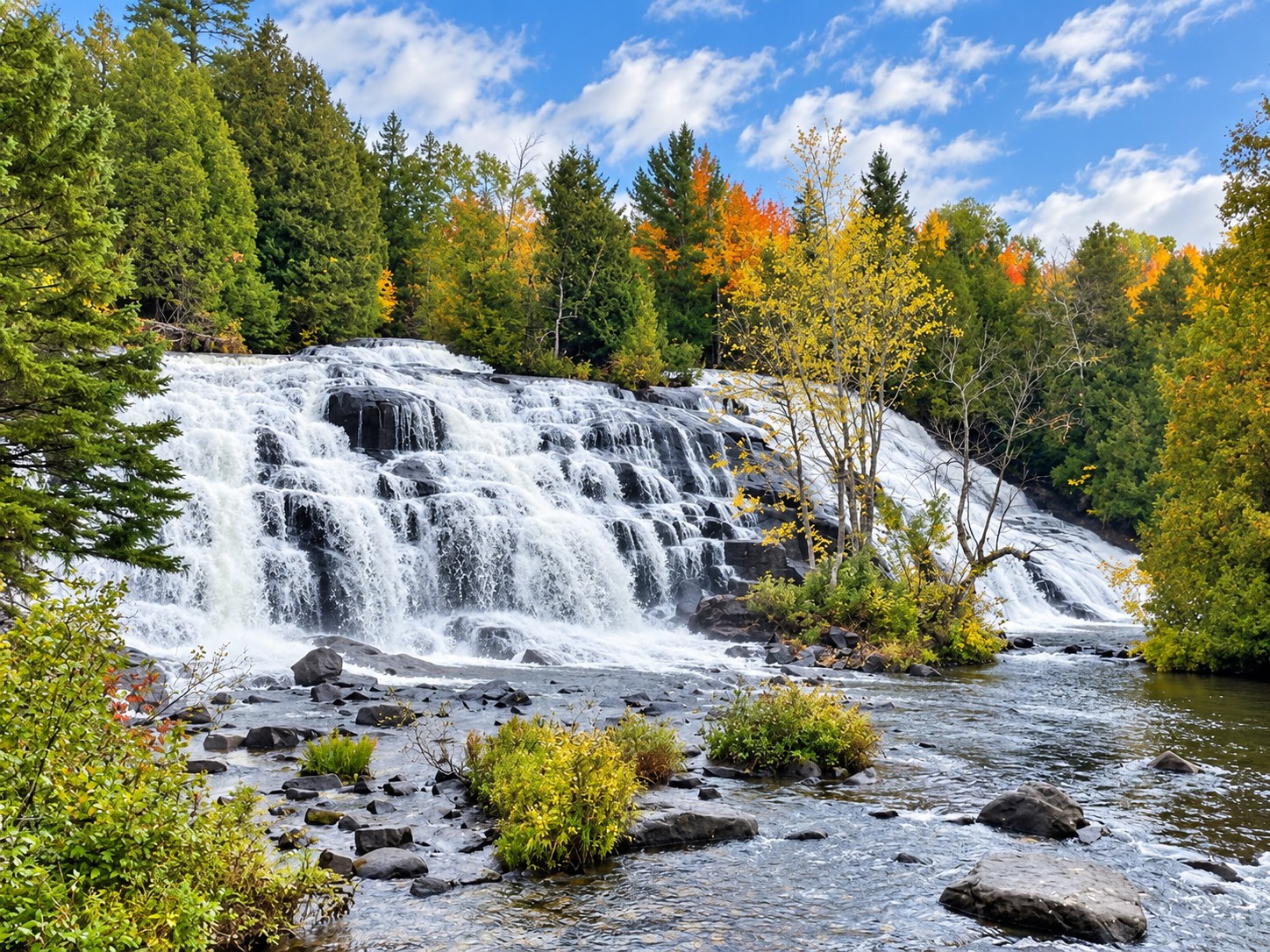Bond Falls in full flow over its rock steps with fall color in the trees behind